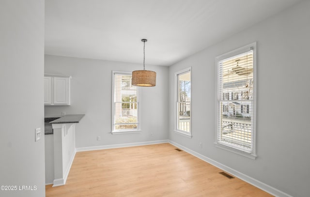 unfurnished dining area with a healthy amount of sunlight, visible vents, light wood finished floors, and baseboards