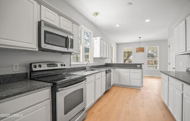 kitchen featuring a peninsula, a sink, stainless steel appliances, white cabinets, and pendant lighting