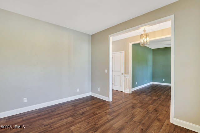 empty room featuring baseboards, a chandelier, and dark wood finished floors
