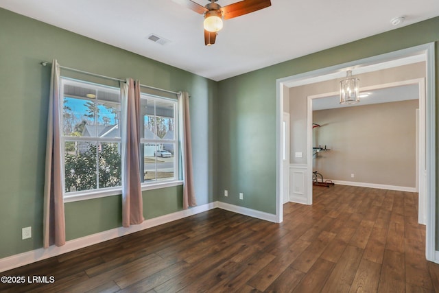 empty room featuring baseboards, dark wood-style flooring, visible vents, and ceiling fan with notable chandelier