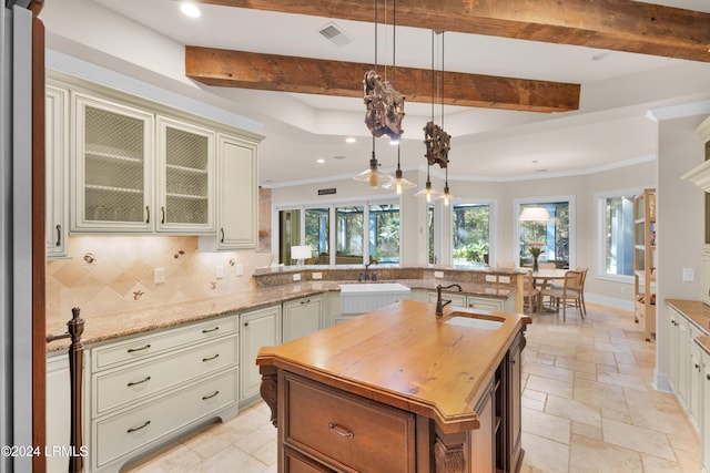 kitchen featuring sink, decorative light fixtures, a center island with sink, light stone countertops, and backsplash