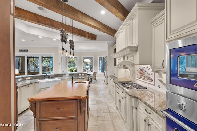 kitchen with sink, hanging light fixtures, a center island with sink, beam ceiling, and light stone countertops