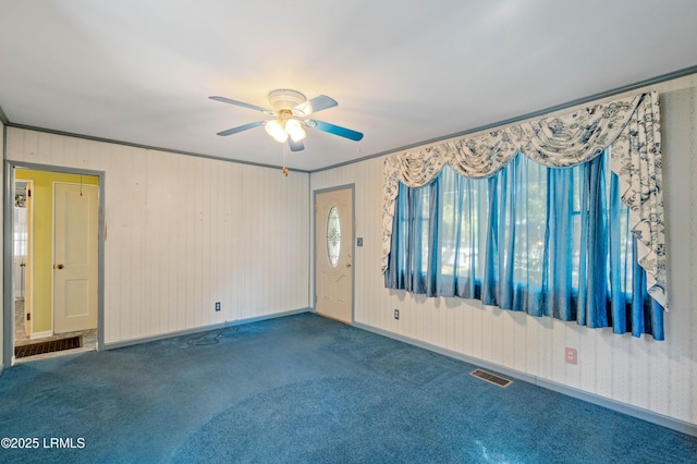 carpeted spare room featuring ceiling fan, visible vents, baseboards, and ornamental molding