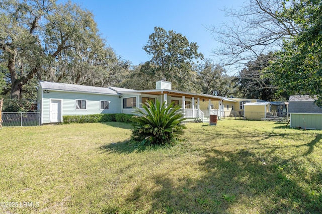 rear view of property with a lawn, fence, covered porch, an outdoor structure, and a chimney