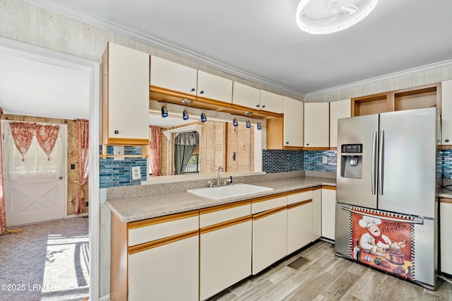 kitchen with a sink, stainless steel fridge, crown molding, light countertops, and decorative backsplash