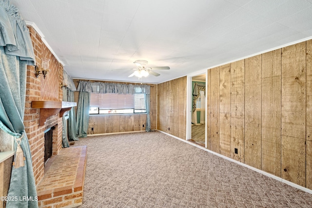 unfurnished living room featuring wood walls, carpet flooring, baseboards, a brick fireplace, and ceiling fan