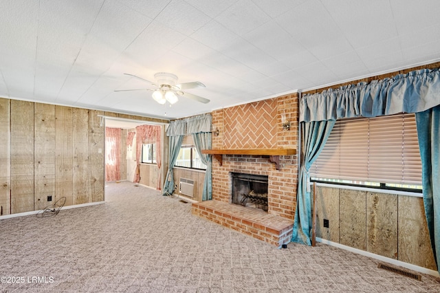 unfurnished living room with visible vents, carpet floors, wooden walls, a brick fireplace, and ceiling fan