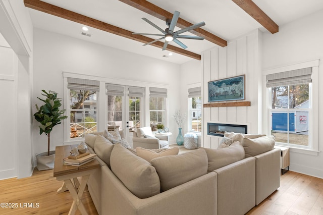 living room featuring ceiling fan, a large fireplace, french doors, beamed ceiling, and light wood-type flooring