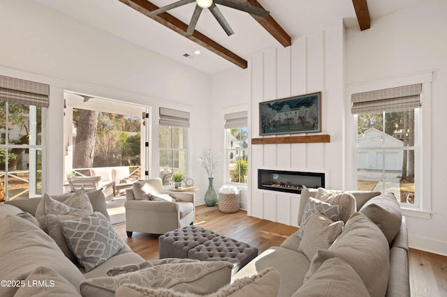 living room featuring a towering ceiling, a fireplace, wood-type flooring, ceiling fan, and beam ceiling