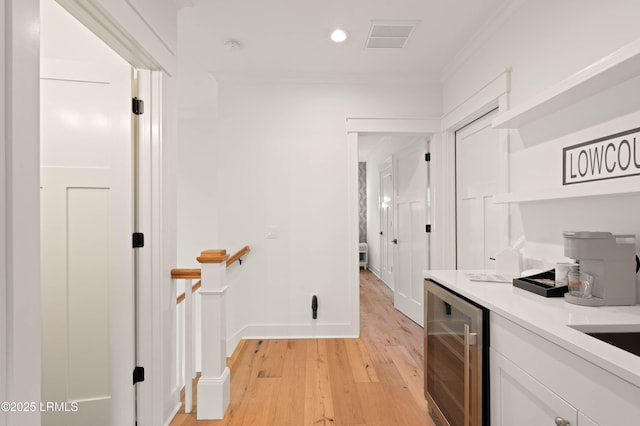 interior space with crown molding, light hardwood / wood-style flooring, beverage cooler, and white cabinets