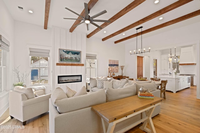 living room featuring beamed ceiling, a fireplace, ceiling fan with notable chandelier, and light hardwood / wood-style flooring