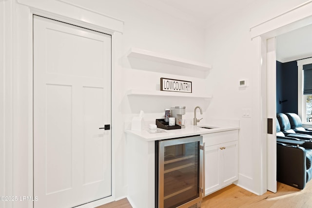 bar with white cabinets, sink, beverage cooler, and light wood-type flooring