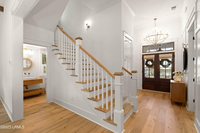 foyer entrance featuring a towering ceiling, light hardwood / wood-style floors, french doors, and a chandelier