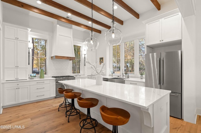 kitchen featuring white cabinetry, decorative light fixtures, premium appliances, a kitchen island, and light stone countertops