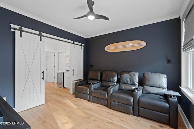 home theater room featuring wine cooler, ornamental molding, a barn door, and light hardwood / wood-style floors