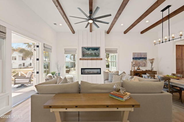 living room with beam ceiling, a fireplace, ceiling fan with notable chandelier, and light wood-type flooring