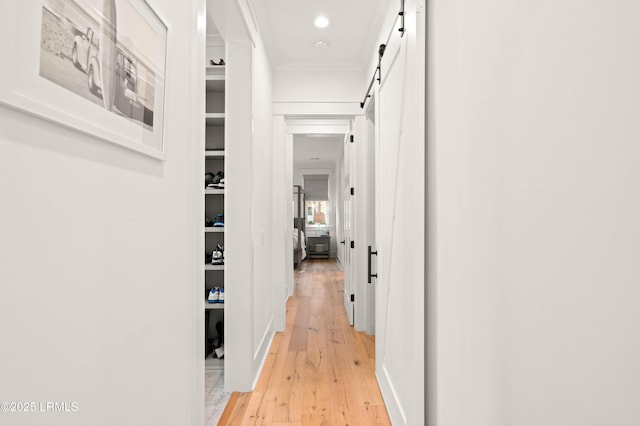 hallway featuring crown molding, a barn door, and light hardwood / wood-style floors