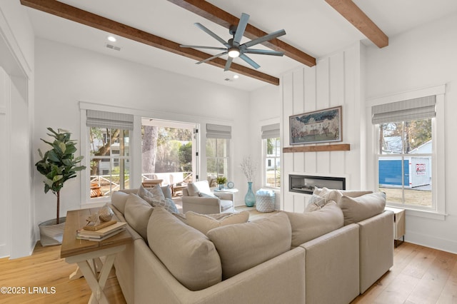 living room featuring a large fireplace, a healthy amount of sunlight, beam ceiling, and light hardwood / wood-style floors