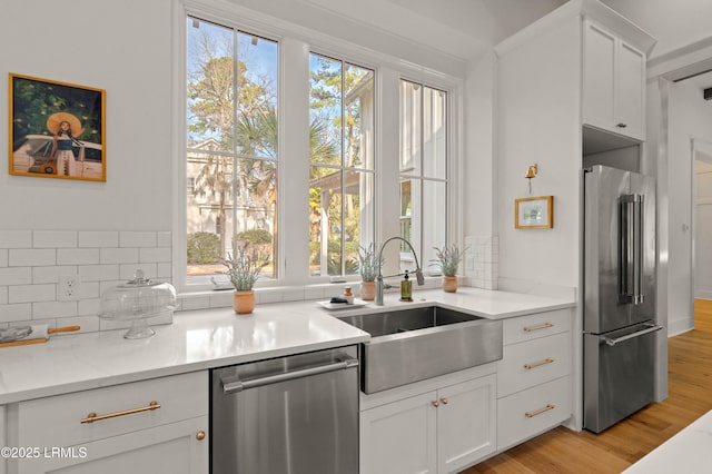 kitchen featuring appliances with stainless steel finishes, sink, backsplash, white cabinets, and light hardwood / wood-style floors