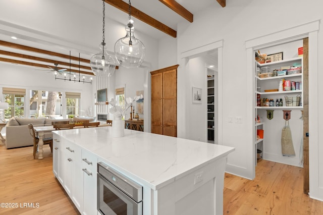 kitchen featuring pendant lighting, a center island, stainless steel microwave, light stone counters, and white cabinets