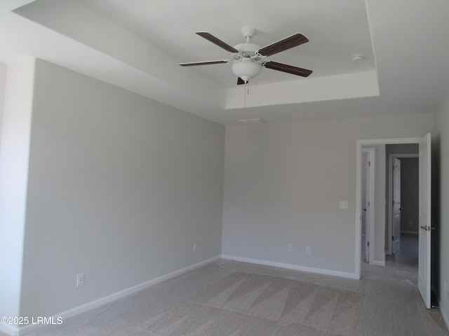 spare room featuring baseboards, a tray ceiling, ceiling fan, and light colored carpet