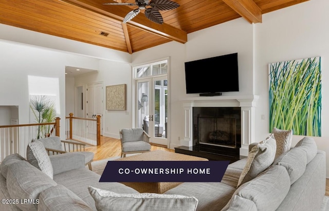 living area featuring a fireplace with raised hearth, lofted ceiling with beams, wood finished floors, baseboards, and wood ceiling