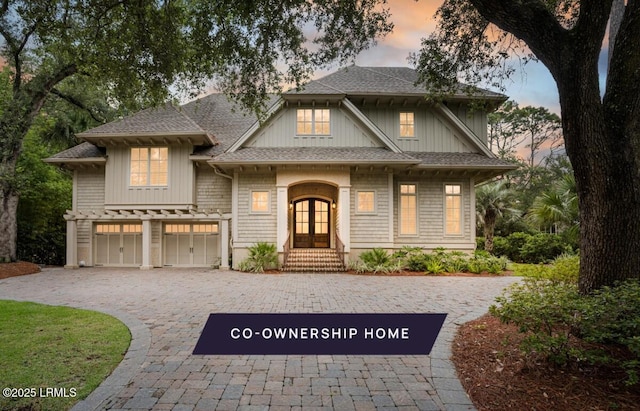 view of front of property featuring decorative driveway, french doors, a garage, and a shingled roof