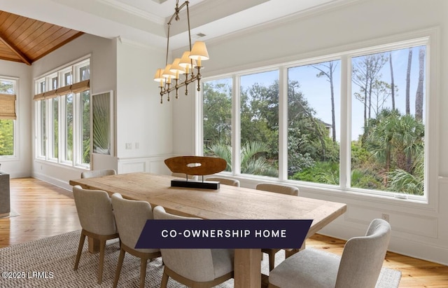 dining room featuring a wainscoted wall, a notable chandelier, light wood-style floors, crown molding, and a decorative wall