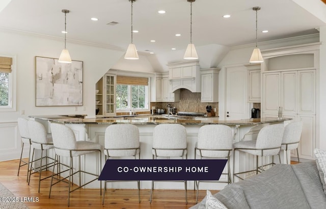 kitchen with visible vents, light wood finished floors, ornamental molding, a kitchen bar, and backsplash