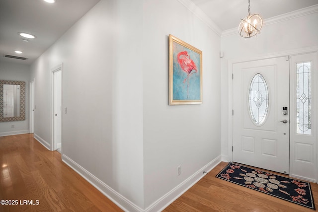 foyer with a notable chandelier, wood finished floors, visible vents, baseboards, and ornamental molding