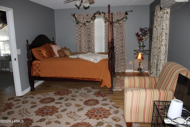 bedroom with ceiling fan, a wall mounted AC, and light hardwood / wood-style floors