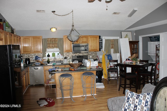 kitchen with vaulted ceiling, a kitchen island, a breakfast bar, decorative backsplash, and stainless steel appliances