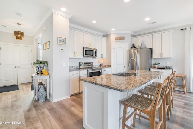 kitchen with sink, appliances with stainless steel finishes, white cabinetry, light stone countertops, and an island with sink