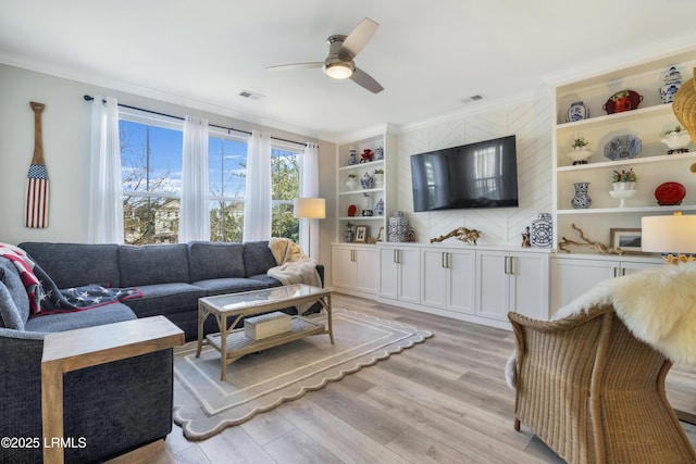 living room featuring built in shelves, ceiling fan, ornamental molding, and light wood-type flooring