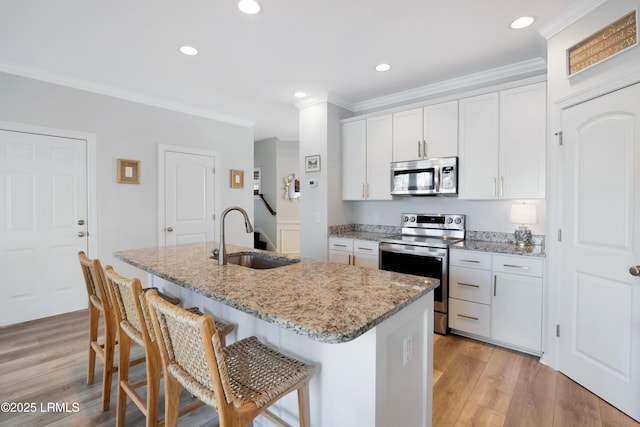 kitchen with sink, appliances with stainless steel finishes, white cabinetry, light stone counters, and an island with sink