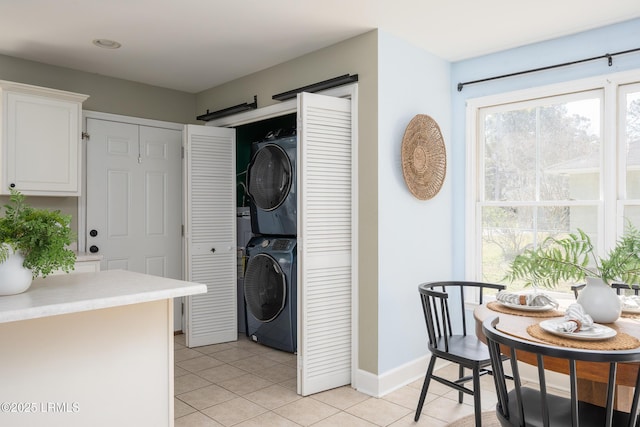 laundry area with laundry area, light tile patterned floors, baseboards, and stacked washer and clothes dryer