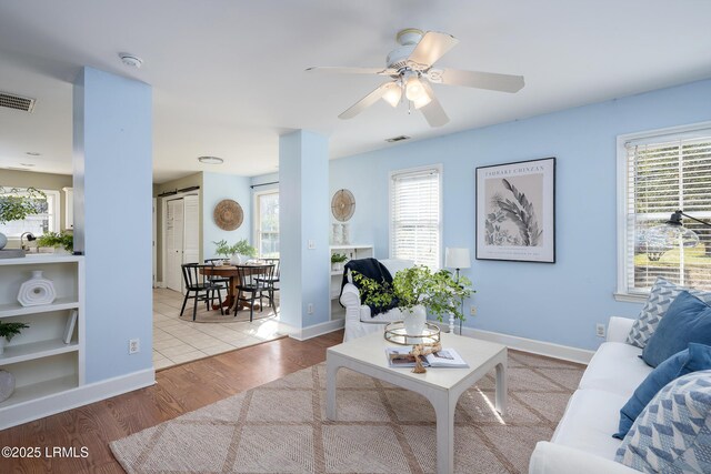 living room featuring light wood-style floors, a wealth of natural light, visible vents, and baseboards