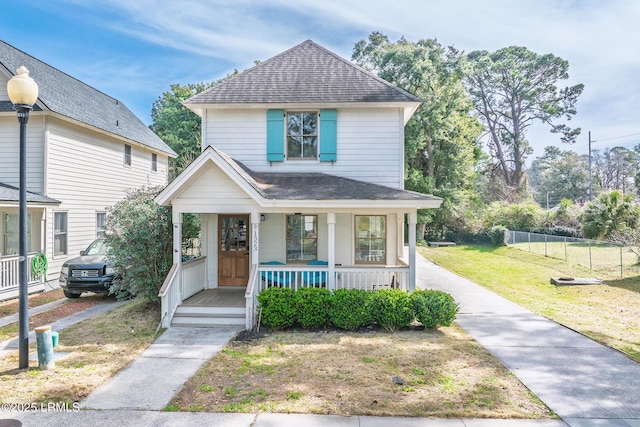 view of front of property featuring roof with shingles, a porch, a front lawn, and fence