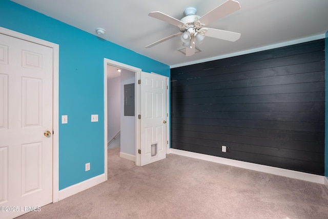 unfurnished bedroom with ceiling fan, carpet floors, an accent wall, wood walls, and baseboards