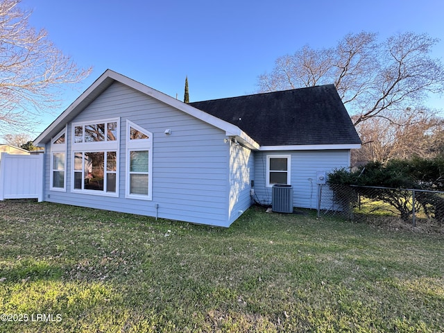 rear view of house featuring central AC, fence, a lawn, and roof with shingles