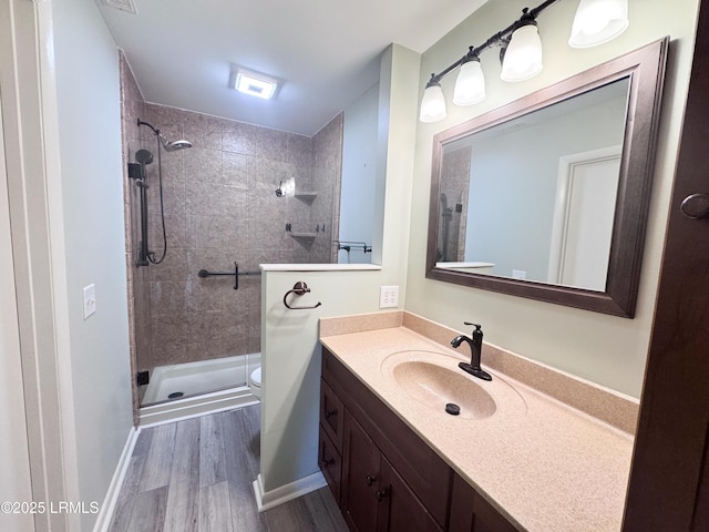 bathroom with toilet, a tile shower, wood finished floors, and vanity