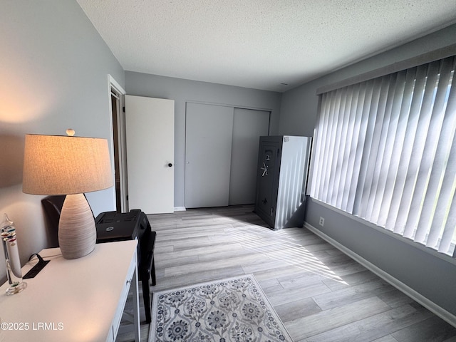 home office featuring a textured ceiling, light wood finished floors, and baseboards