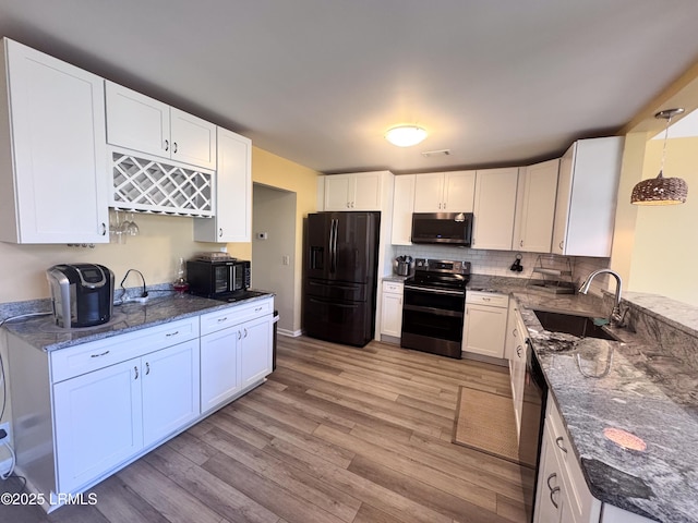 kitchen with a sink, white cabinets, black appliances, light wood finished floors, and dark stone countertops