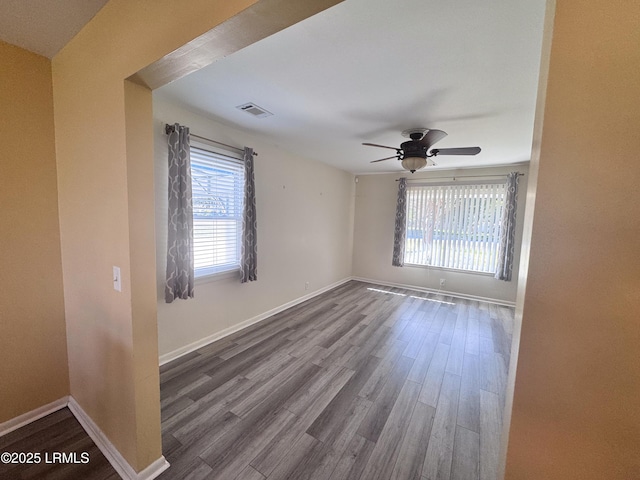 unfurnished room with a ceiling fan, wood finished floors, visible vents, and baseboards