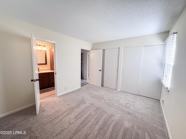 unfurnished bedroom featuring light carpet, a textured ceiling, baseboards, and two closets