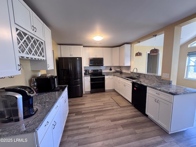 kitchen with a sink, white cabinets, dark stone counters, black appliances, and light wood finished floors