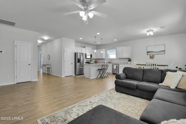 living room featuring ceiling fan, sink, and light wood-type flooring