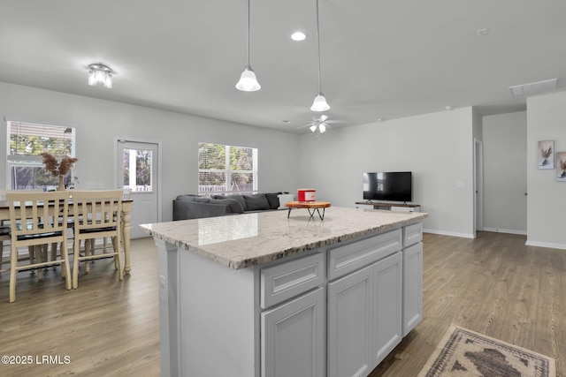 kitchen featuring light stone counters, decorative light fixtures, light hardwood / wood-style flooring, a kitchen island, and ceiling fan