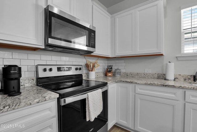 kitchen with stainless steel appliances, white cabinetry, light stone countertops, and tasteful backsplash