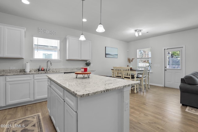 kitchen featuring sink, a center island, light hardwood / wood-style flooring, hanging light fixtures, and white cabinets